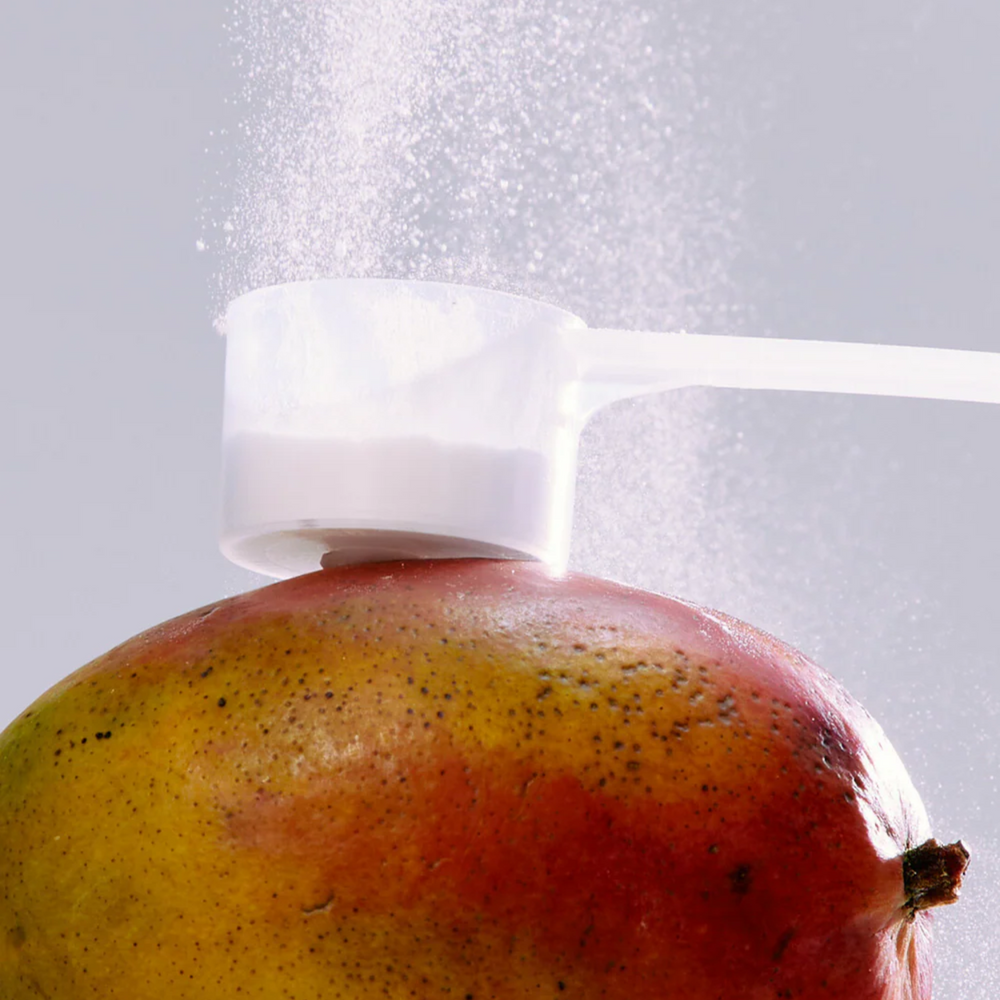 Poudre du supplément Grow & Glow saveur pêche et mangue, pot posé sur fond clair
