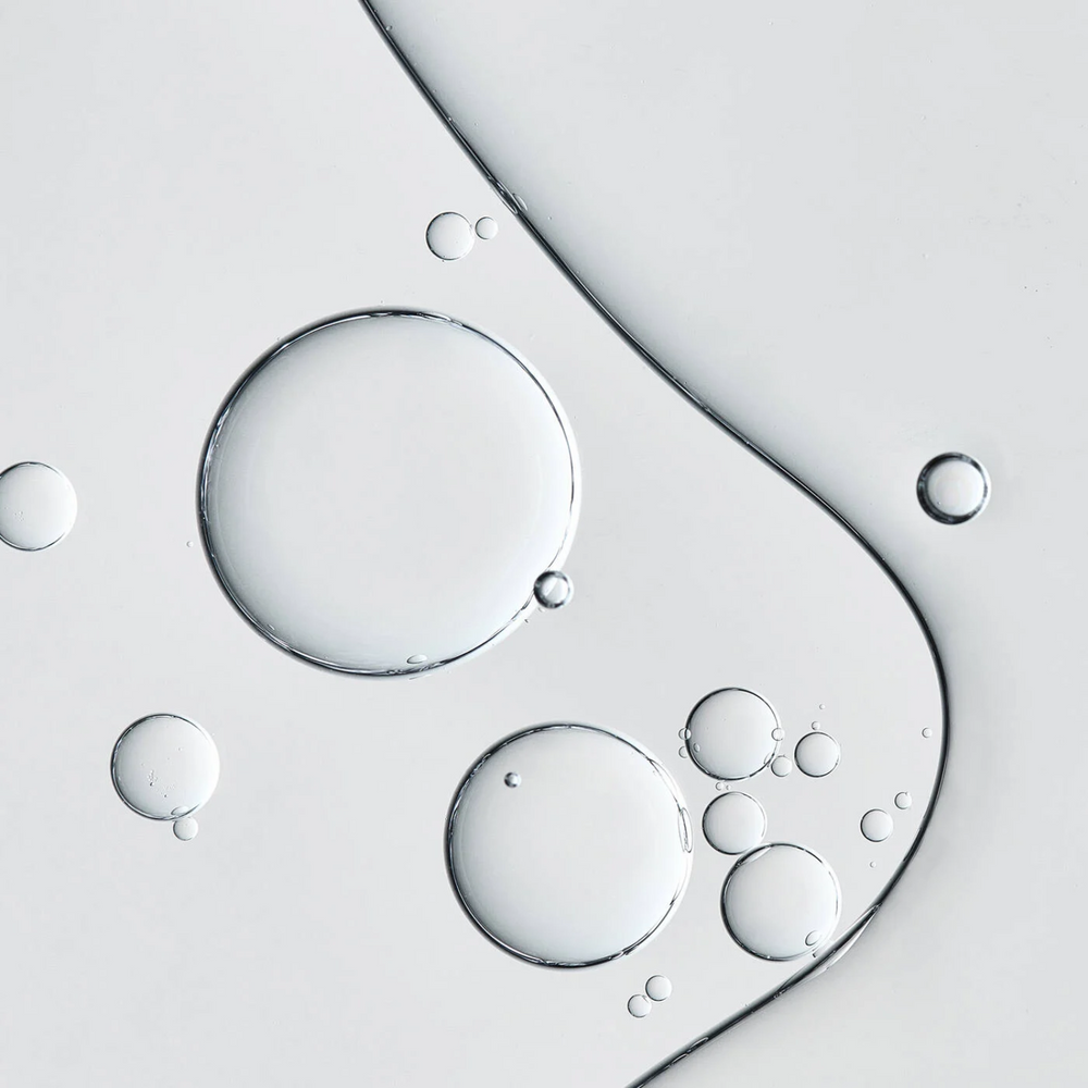 Flacon d’huile capillaire Pureology Hydrate Glow Catcher Oil posé sur une surface neutre.