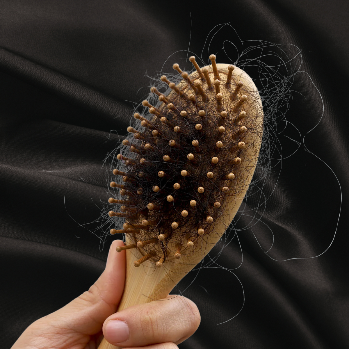 Brosse avec beaucoup de cheveux (perte de cheveux) tenu par une main sur un fond noir texture satin