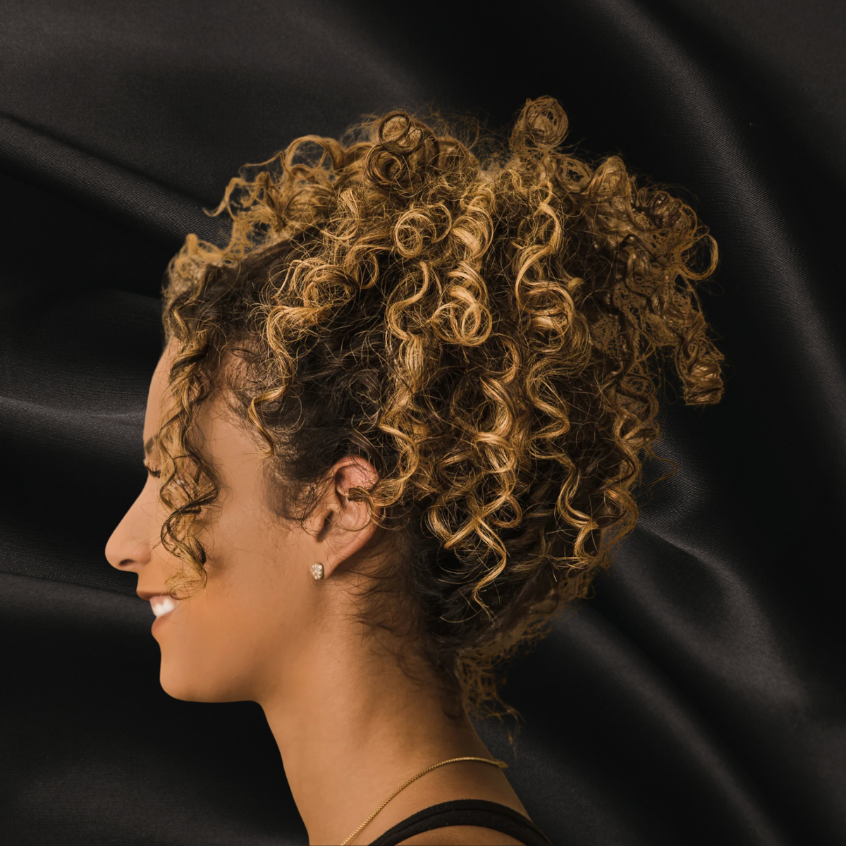 Femme de profil avec beau cheveux frisés sur fond noir texture satin
