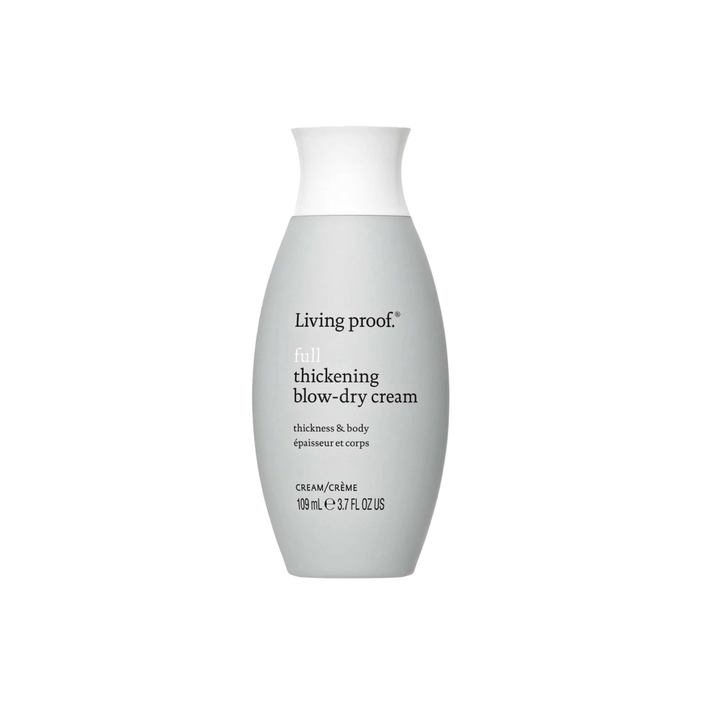 Flacon de crème coiffante Living Proof posé sur une surface claire avec des cheveux brillants et volumineux en arrière-plan

