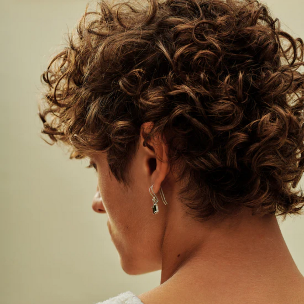 Flacon de AG Beach Bomb Wave‑Enhancing Cream, cheveux ondulés effet plage en arrière-plan