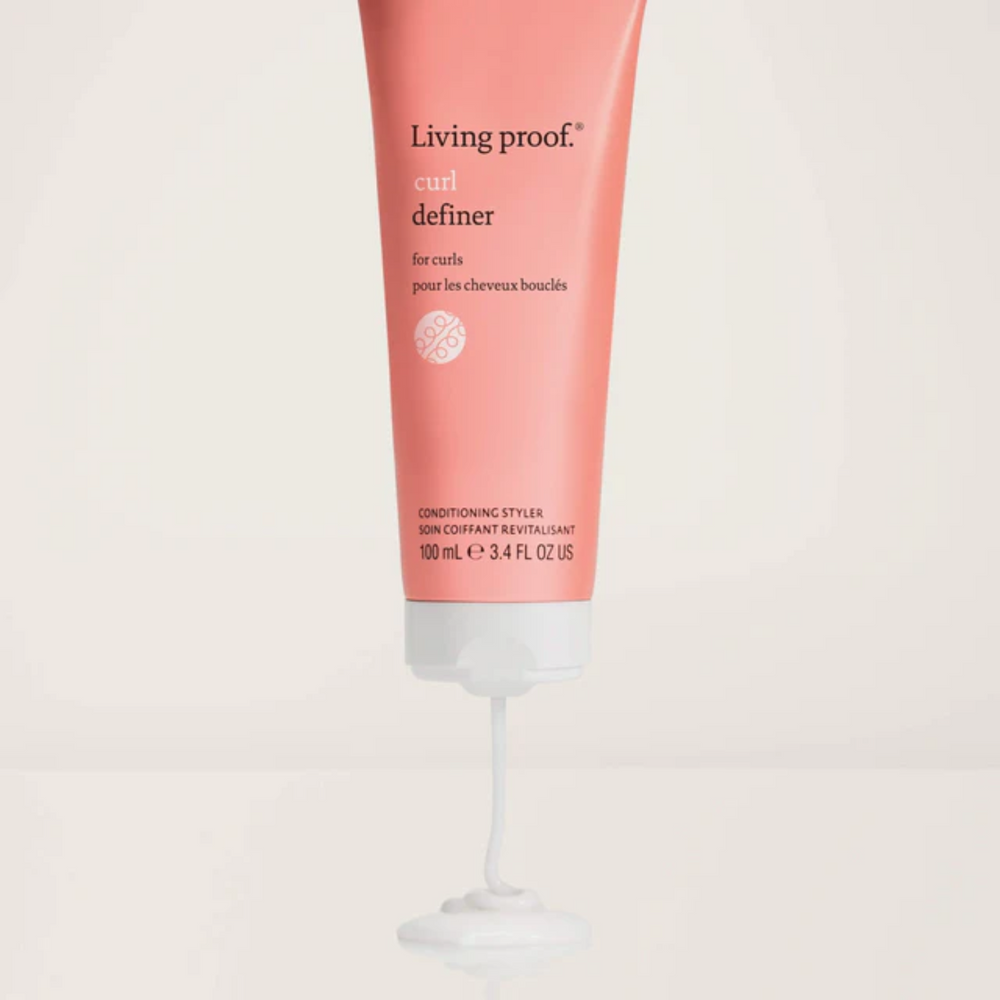 Tube corail du Curl Definer Living Proof avec pompe blanche, posé sur fond clair et montrant sa texture lisse et son design épuré.

