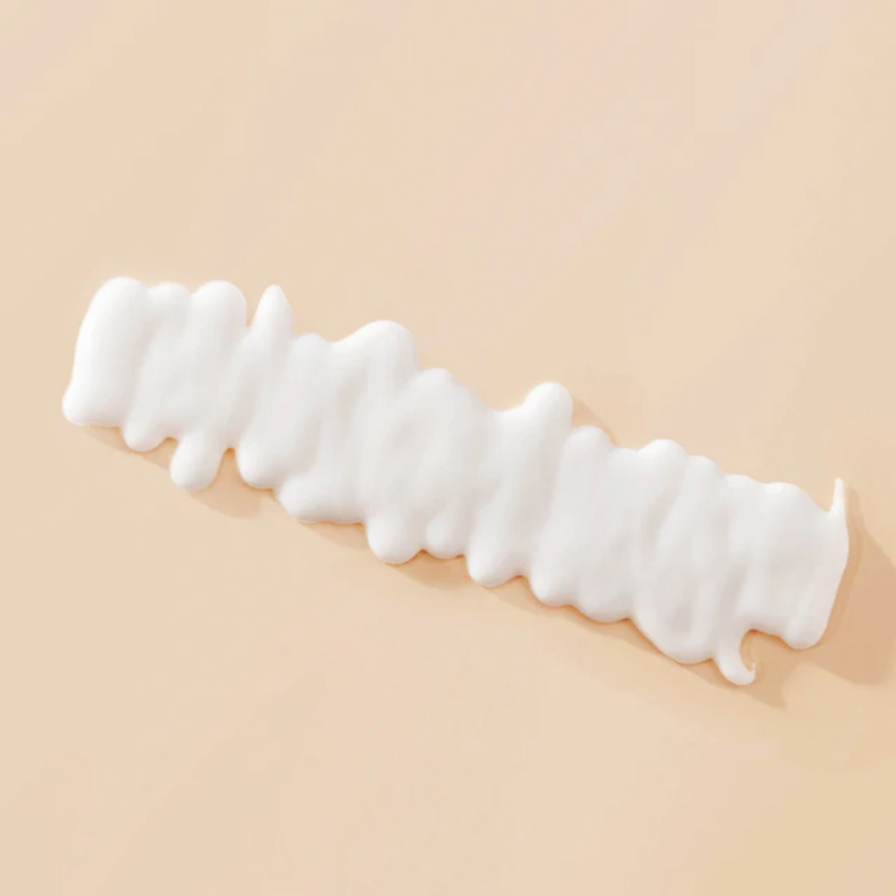 Tube corail du Curl Definer Living Proof avec pompe blanche, posé sur fond clair et montrant sa texture lisse et son design épuré.

