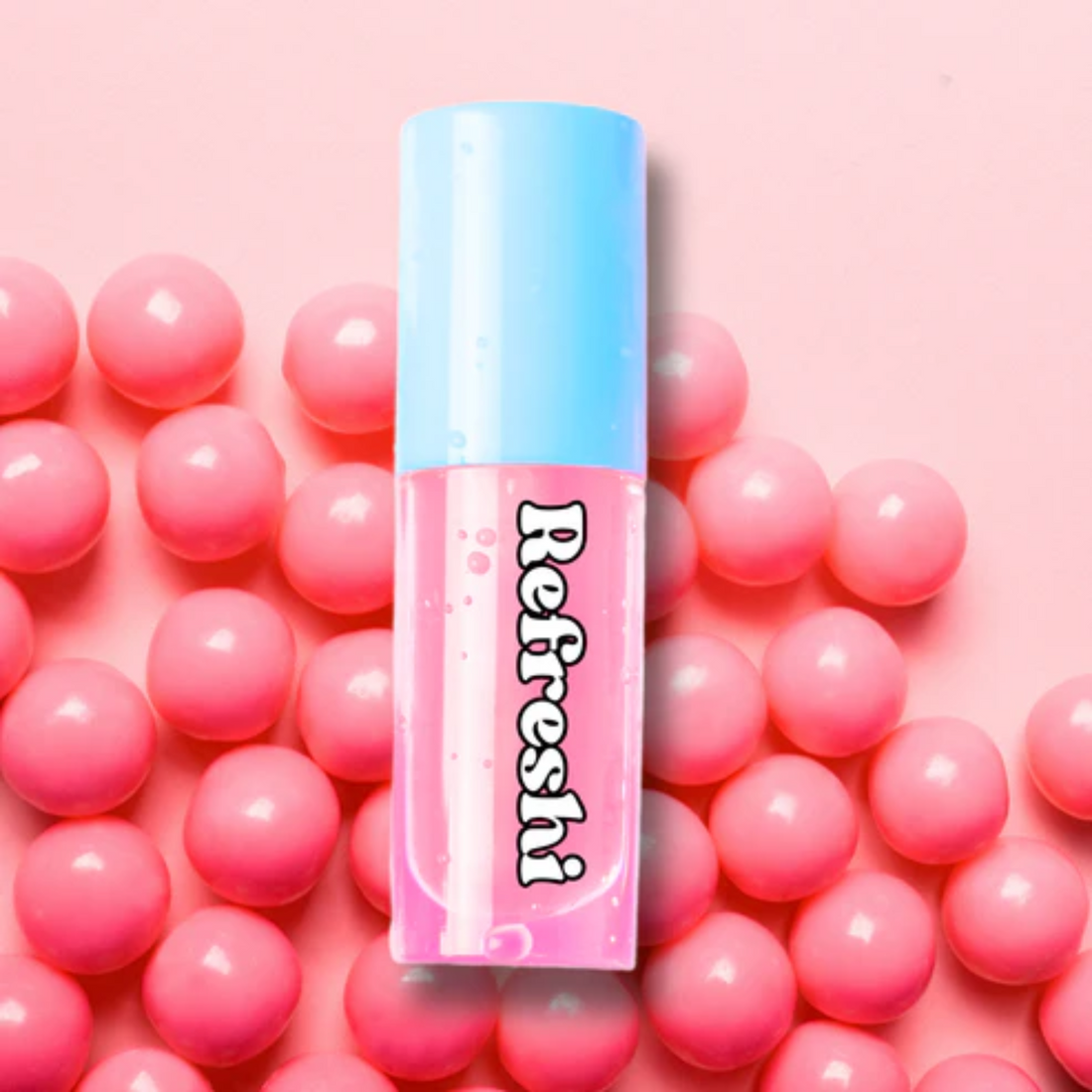 Tube d’huile à lèvres Bubble Gum rose posée sur fond de bonbons, effet brillant et gourmand