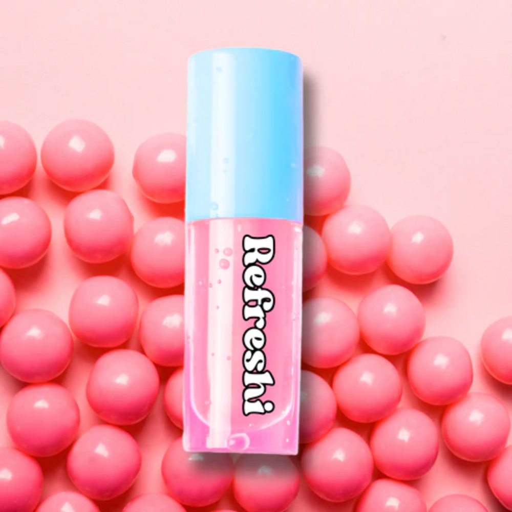 Tube d’huile à lèvres Bubble Gum rose posée sur fond de bonbons, effet brillant et gourmand