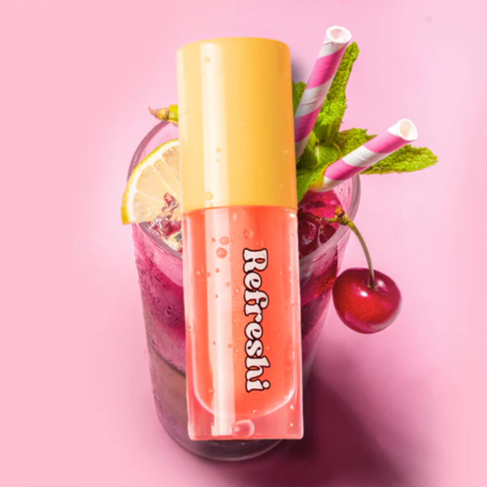 Tube d’huile à lèvres Cherry Lemonade Refreshi sur fond rose, accompagné de fruits cerise et citron, fini glossy fruité

