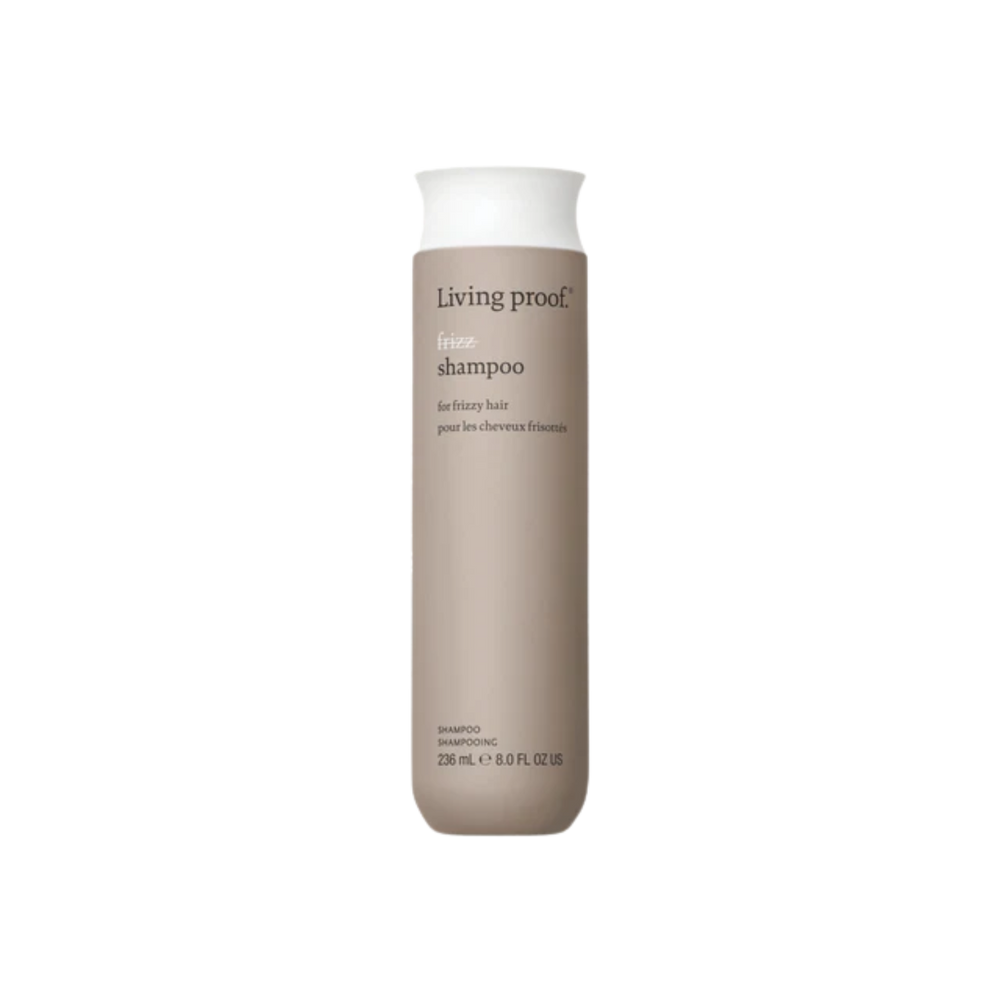 Flacon du shampoing No Frizz Living Proof blanc argenté, évoquant douceur, lissage et anti‑humidité, posé sur un fond clair minimaliste.

