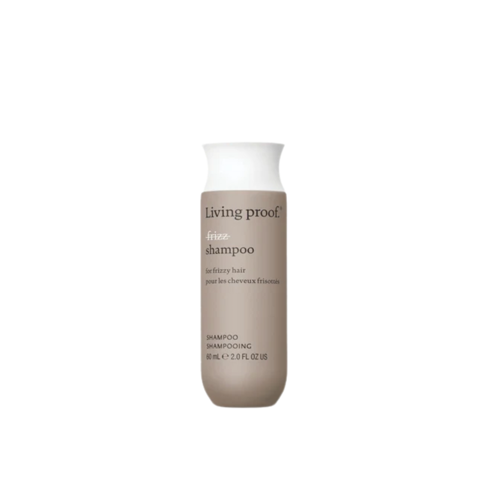 Flacon du shampoing No Frizz Living Proof blanc argenté, évoquant douceur, lissage et anti‑humidité, posé sur un fond clair minimaliste.

