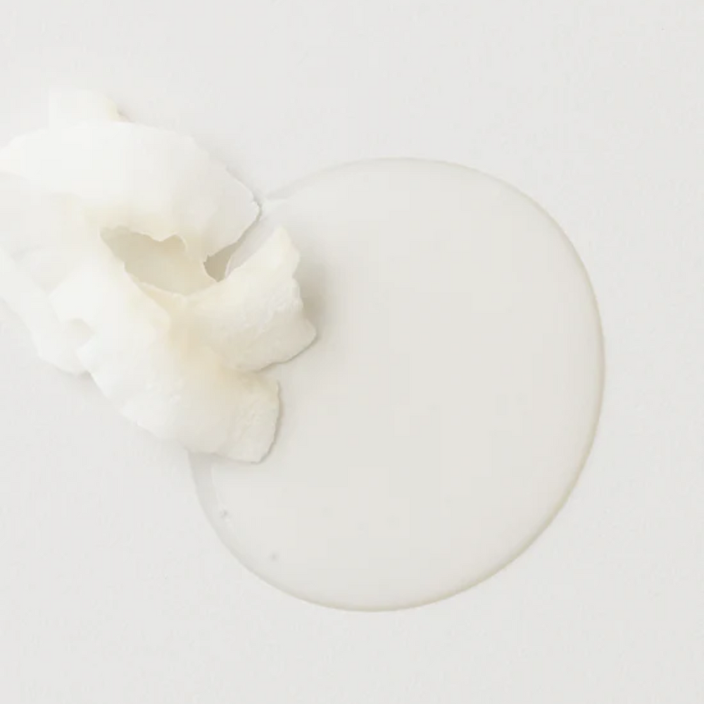 Revitalisant AG Care Sleeek Argan & Coconut, bouteille sur fond neutre, cheveux lisses et brillants en arrière-plan