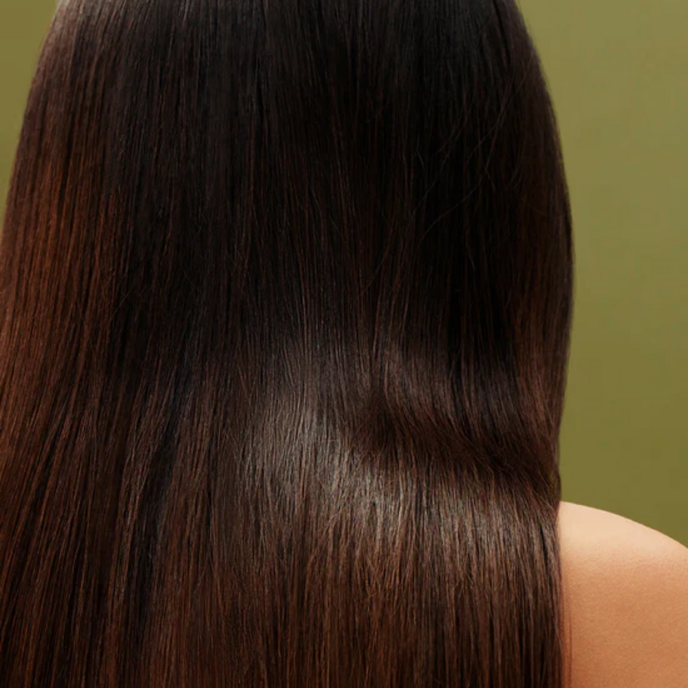 Revitalisant AG Care Sleeek Argan & Coconut, bouteille sur fond neutre, cheveux lisses et brillants en arrière-plan