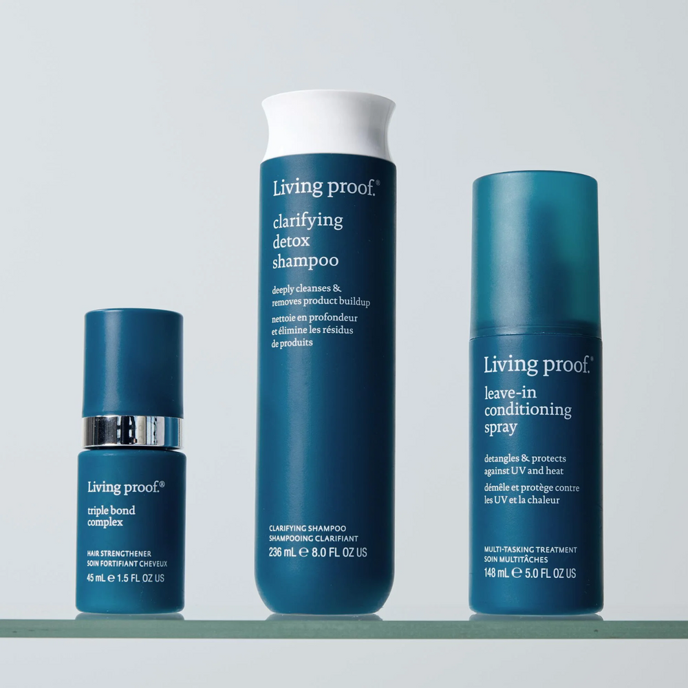 Flacon de spray sans rinçage Living Proof posé sur une surface claire, avec un fond neutre et des cheveux démêlés en arrière-plan

